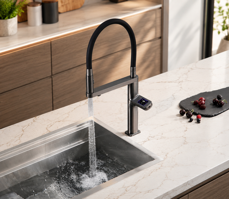 A modern kitchen sink with a tall matte black gooseneck faucet running water, set into a light marble countertop with wooden cabinets in the background.